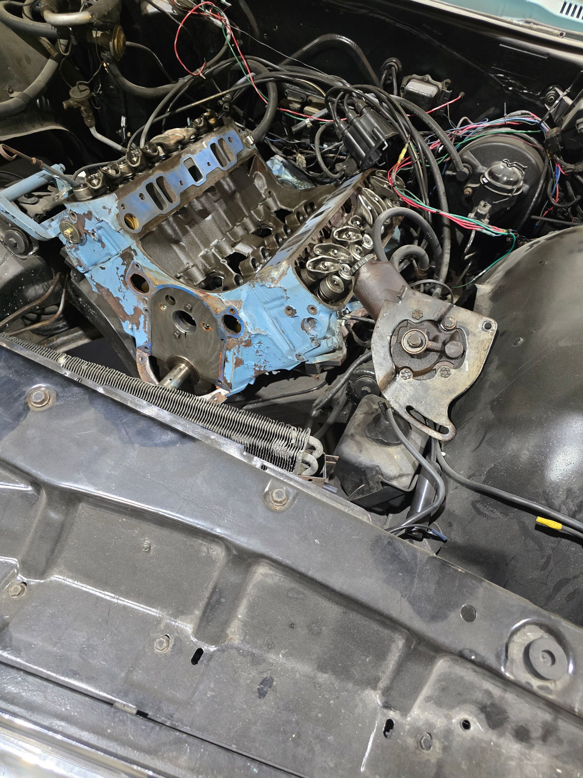 Close-up of a car engine bay with a blue engine block, exposed wires, and disassembled parts