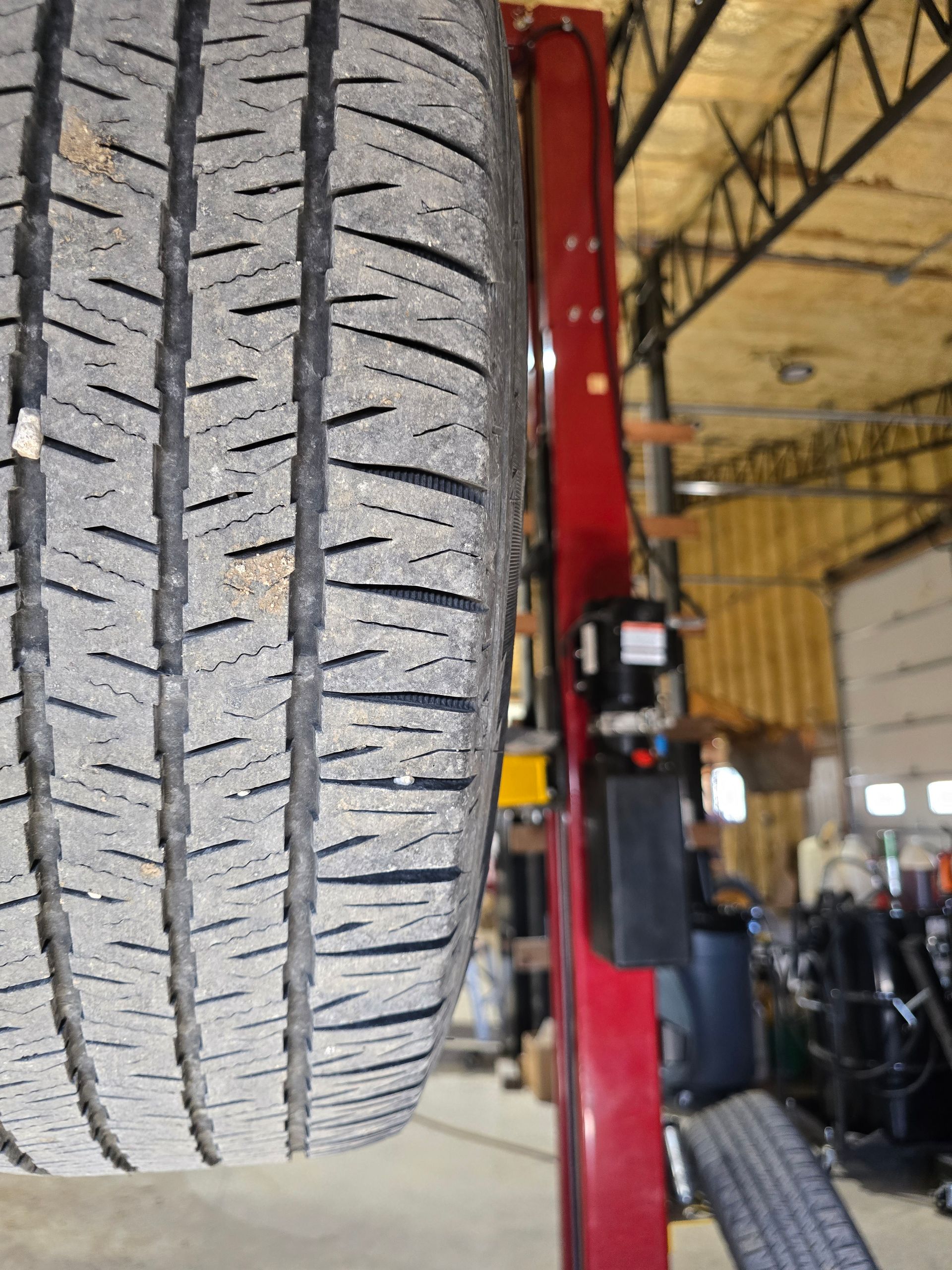 Close-up of a tire tread in a garage with a red vehicle lift in the background