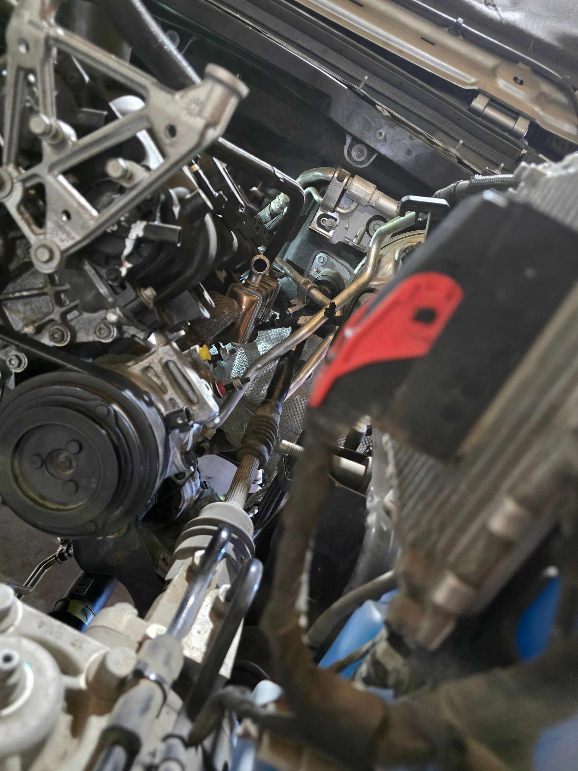 Close-up of a car engine bay with exposed metal parts, hoses, and a red component on the right.