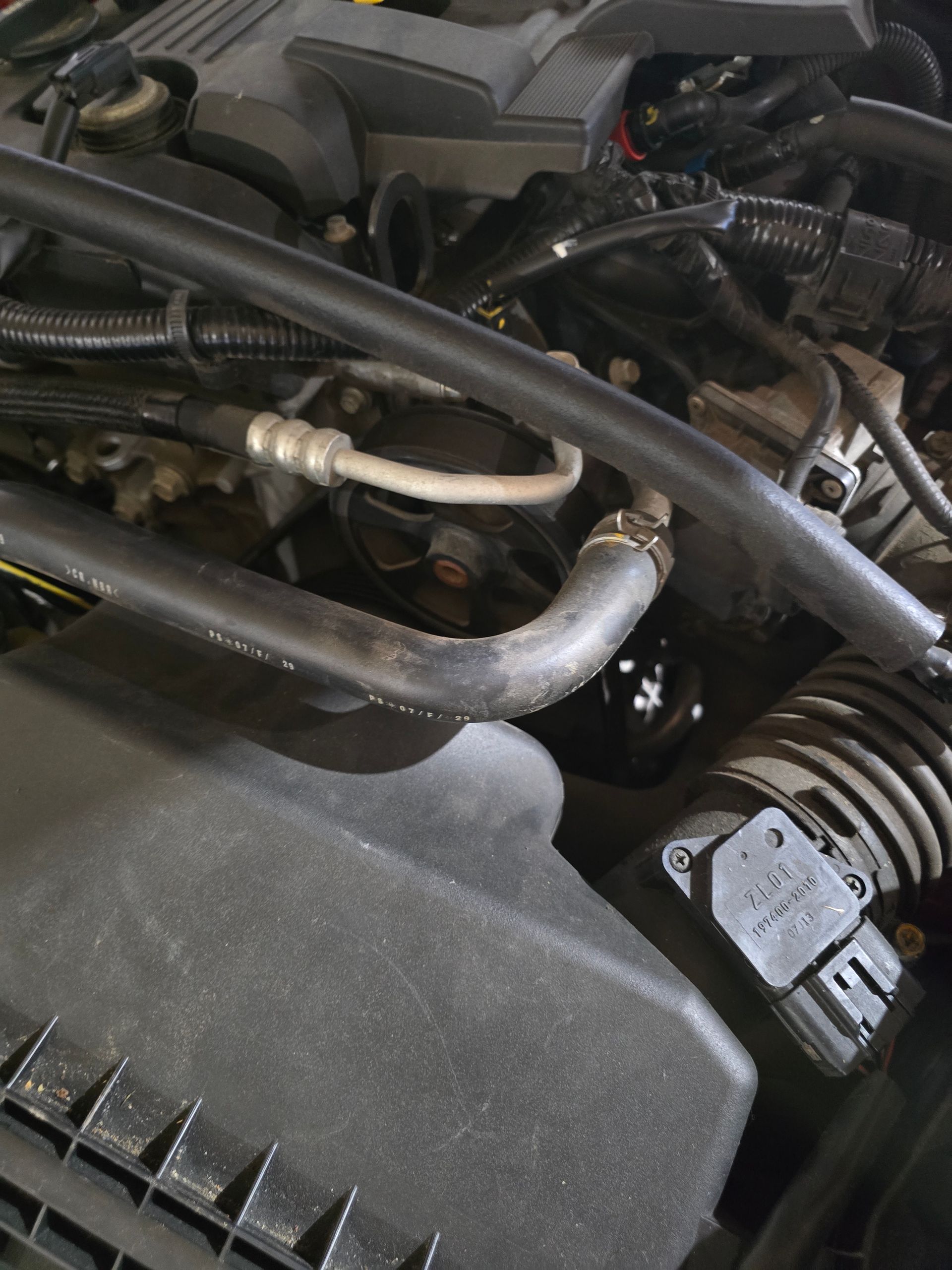 Close-up of a car engine bay with hoses, wiring, and metal pipes.