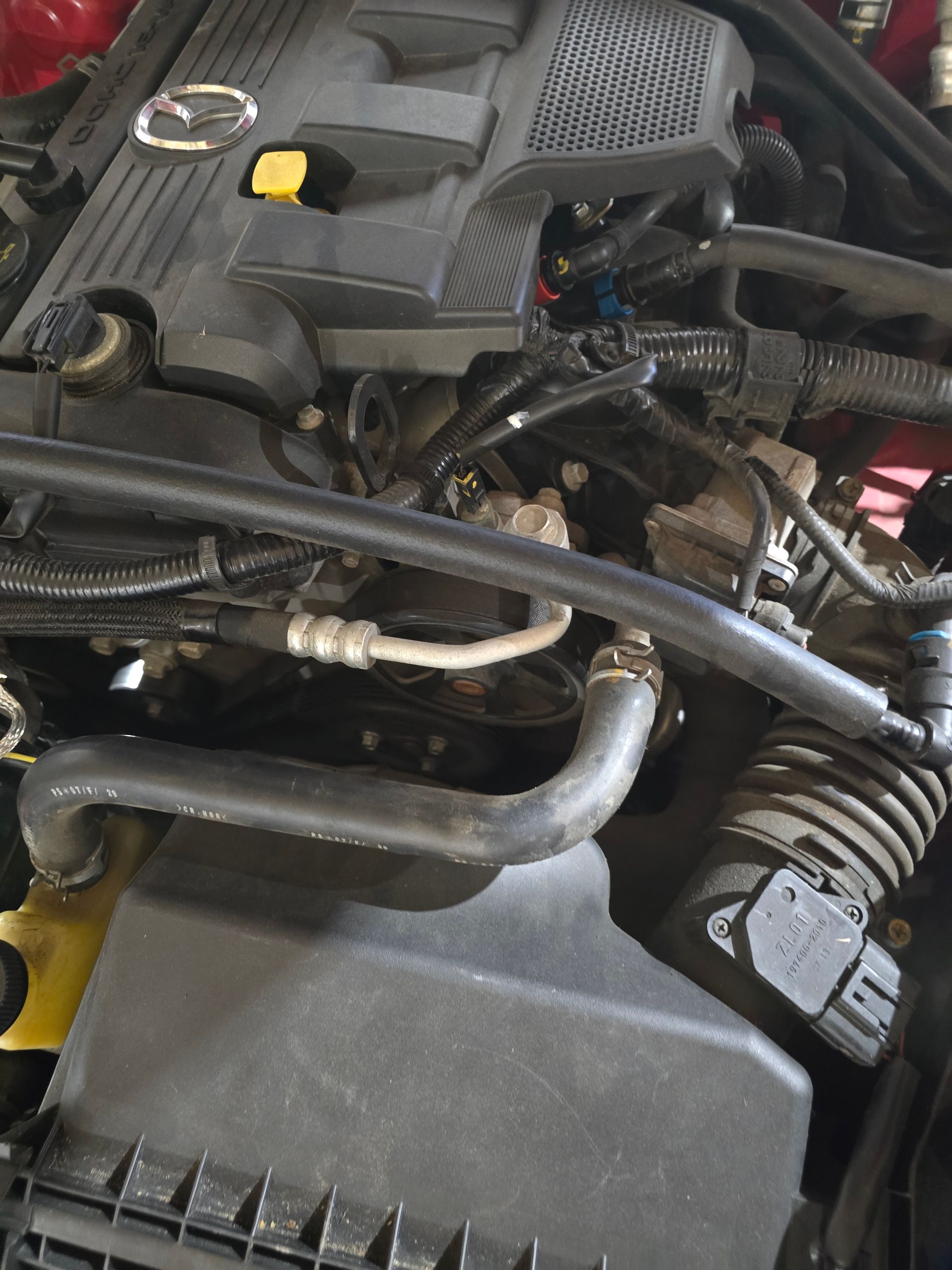 Close-up of a car engine bay with black hoses, a yellow cap, and silver components.