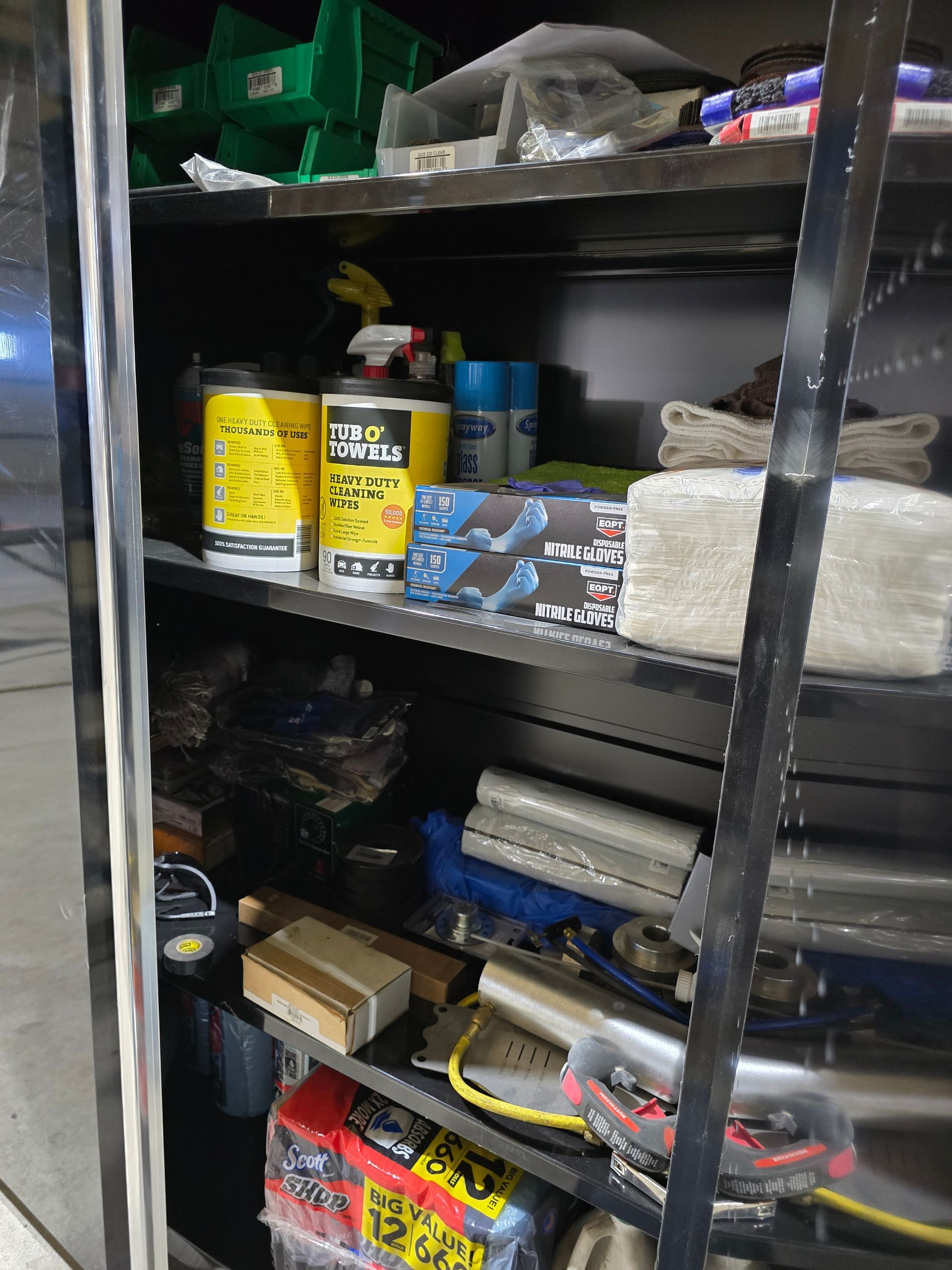 A cluttered metal shelf with paint cans, boxes, and assorted tools in a storage area.