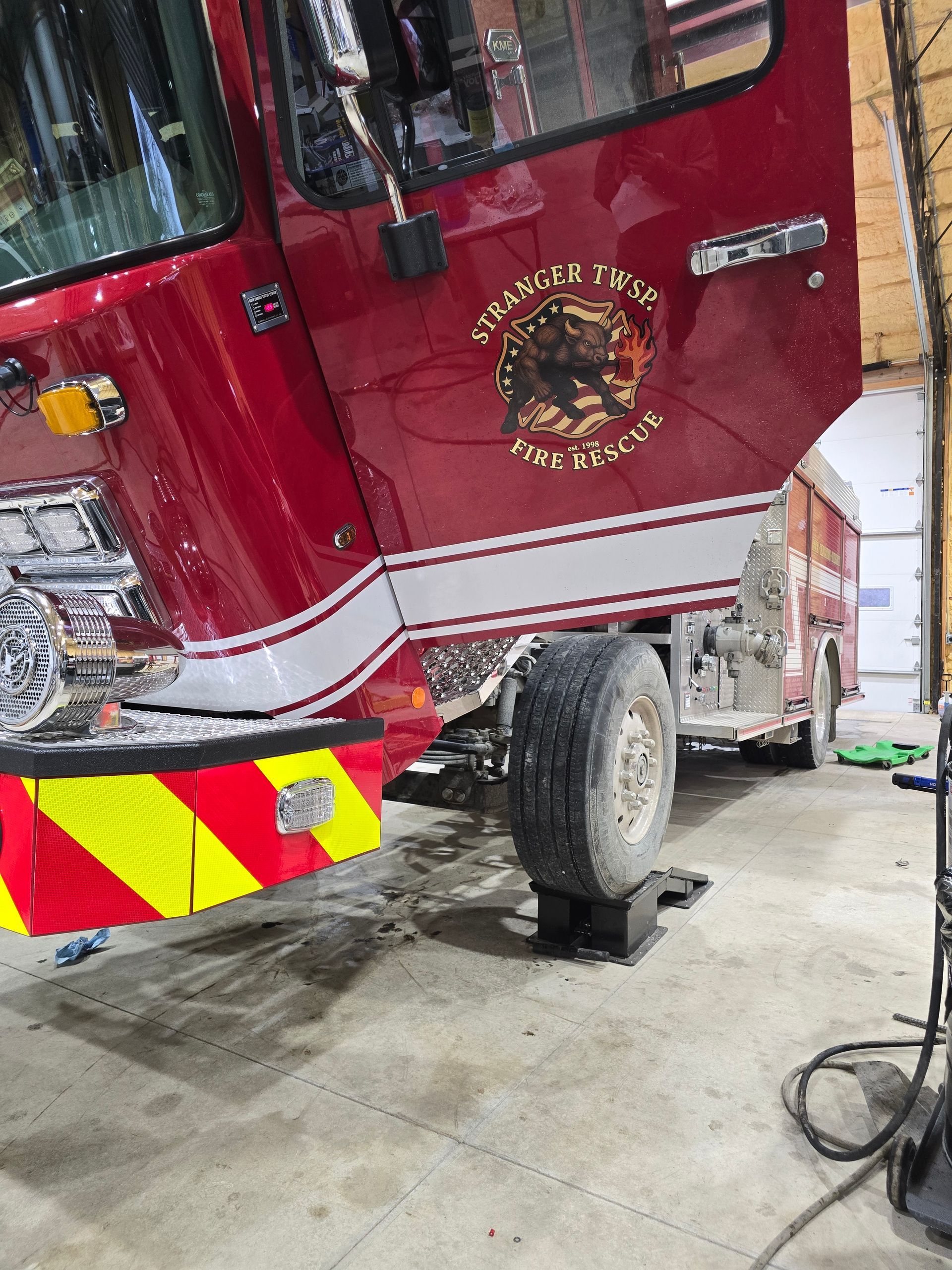 Red fire truck lifted on a jack in a garage, with wheel removed and reflective chevron panel visible