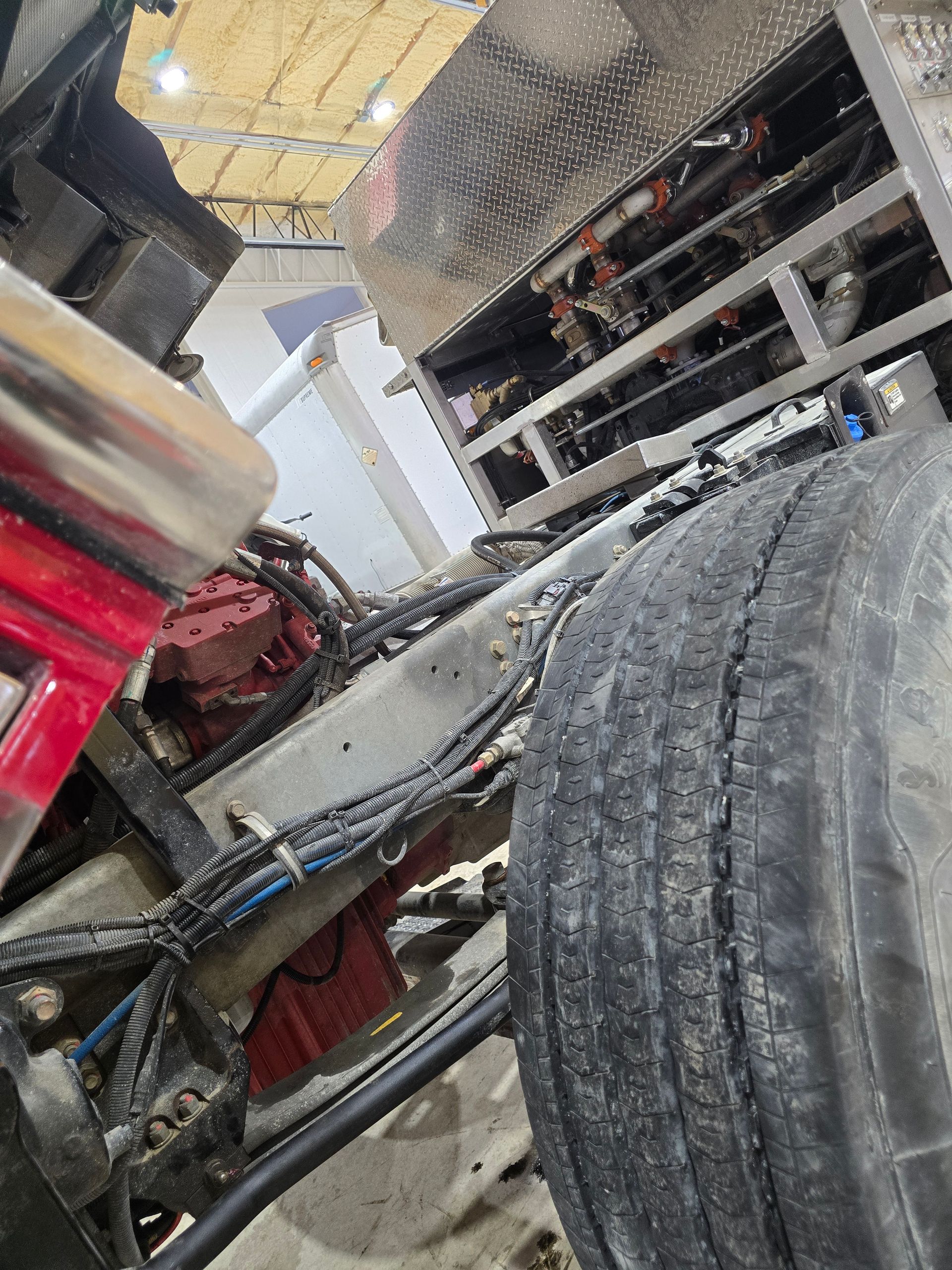 Close-up of a vehicle tire and undercarriage inside a garage, with a red machine and shelves in the background