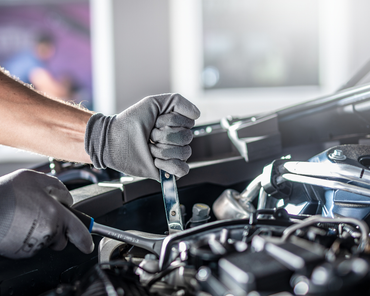 Mechanic's hands in gloves working on a car engine with wrenches.