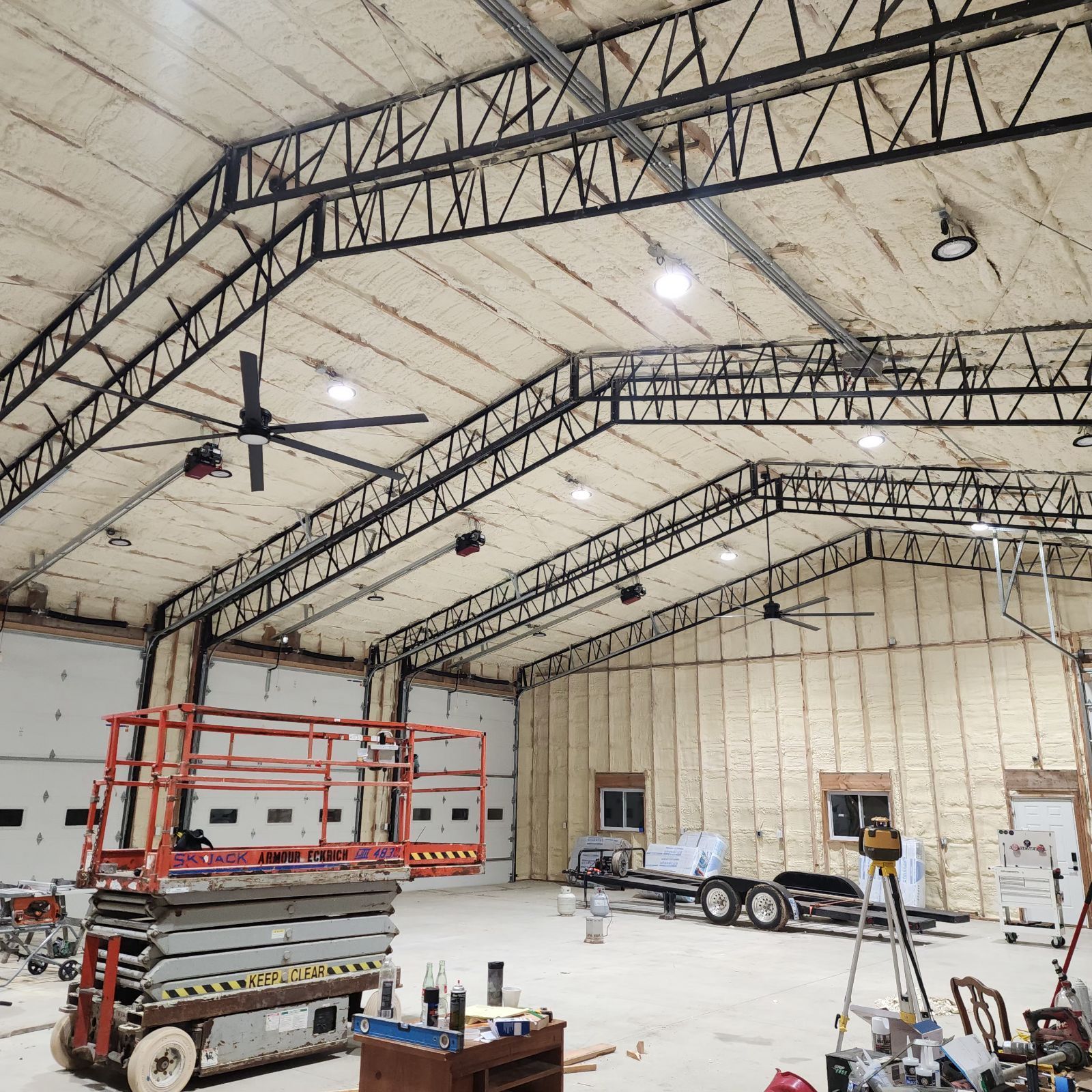 Interior of a large building with exposed black trusses, insulated walls, and a lift.