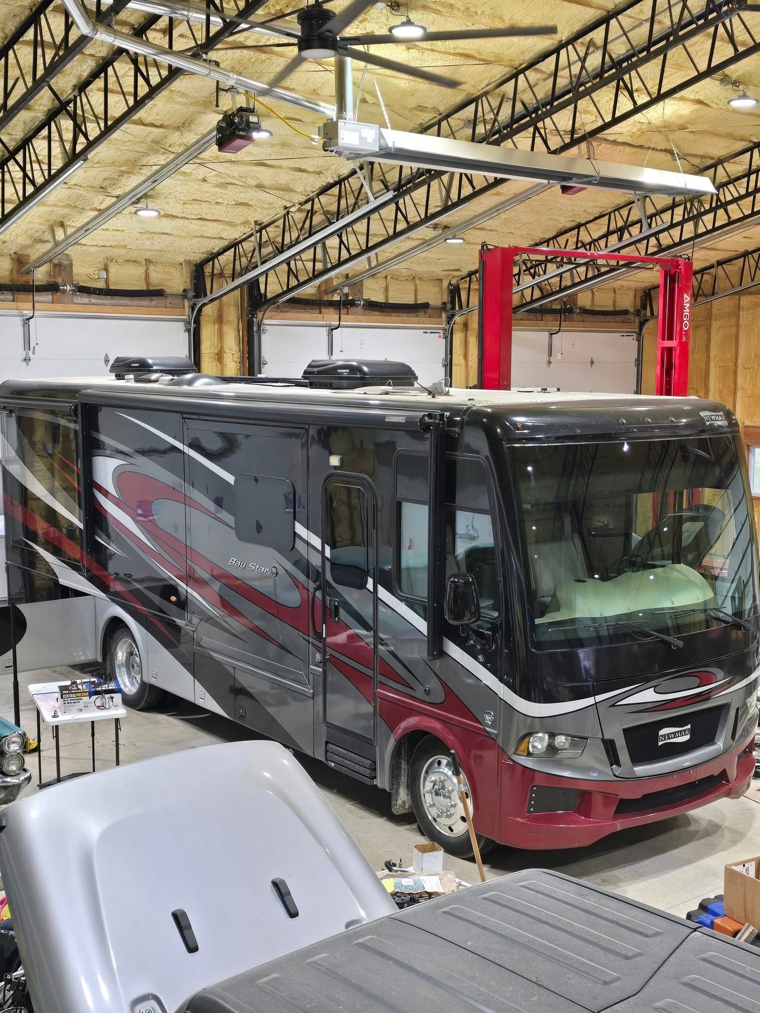 RV in a large garage with high ceilings and a red lift.