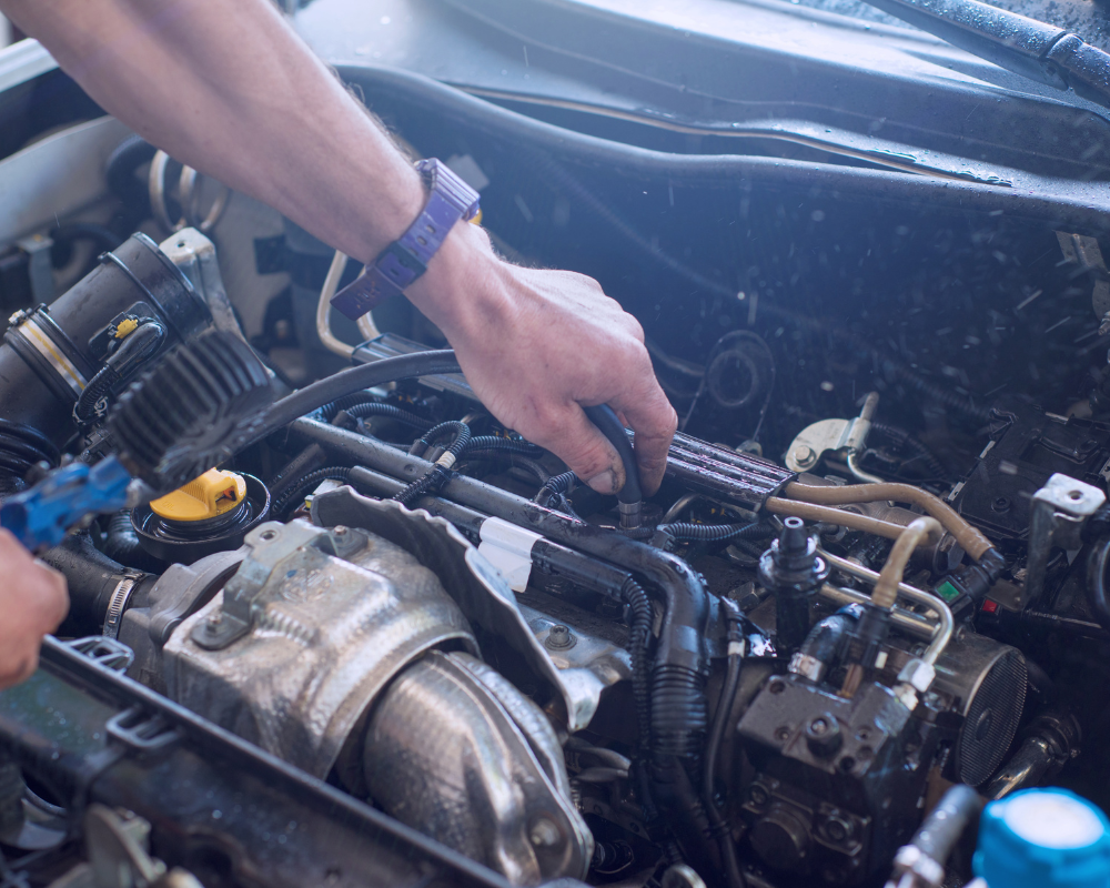 Person washing a car engine bay with a spray bottle, hands visible.