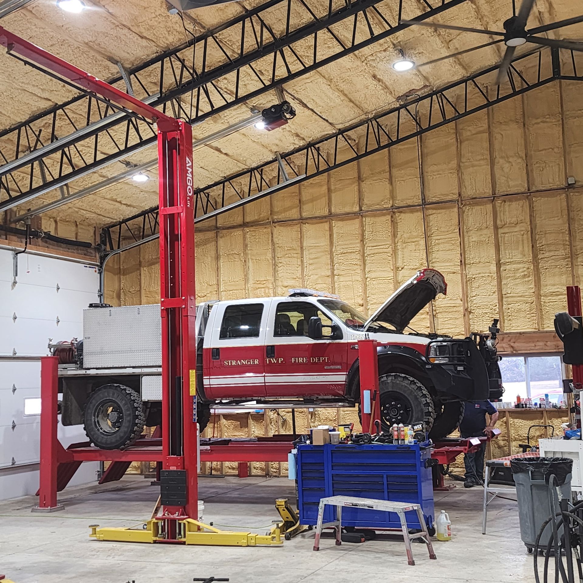 Mechanic in blue overalls climbs into a large blue truck cab, working in a garage setting.
