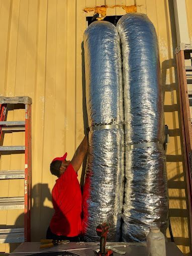 a man in a red shirt is working on a duct on the side of a building .