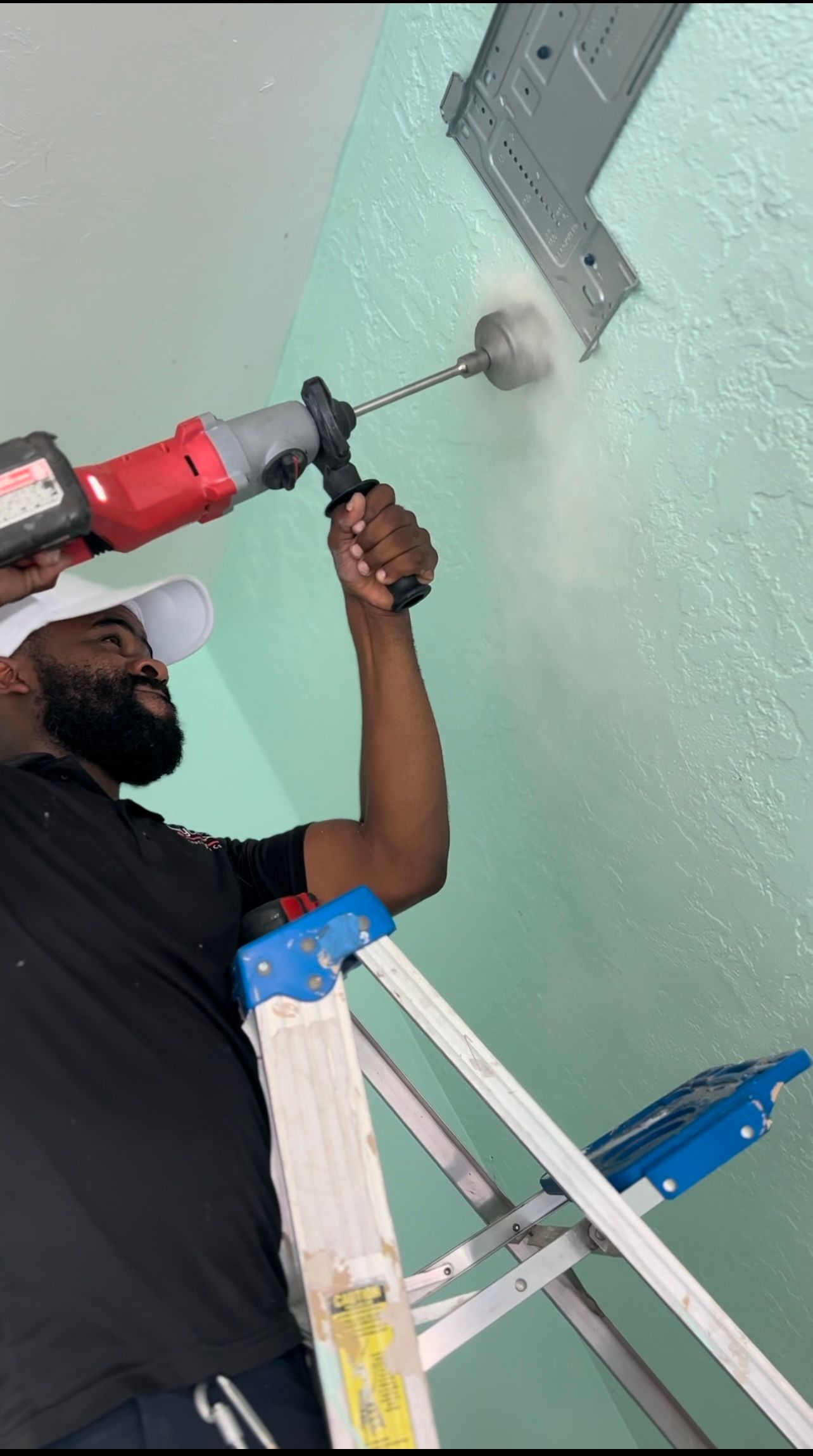 a man is standing on a ladder using a drill to drill a hole in a wall .