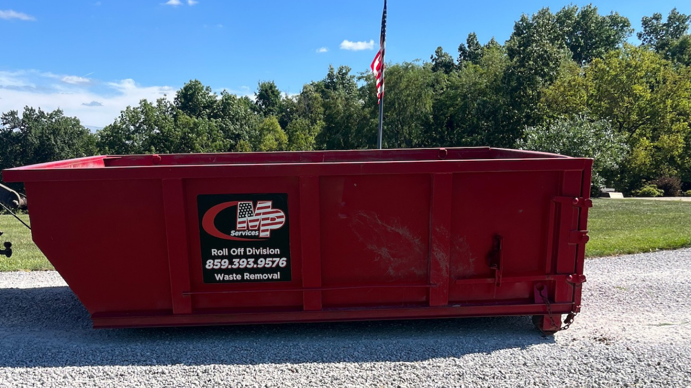 Red dumpster on a gravel driveway with a company logo and an American flag in the background.