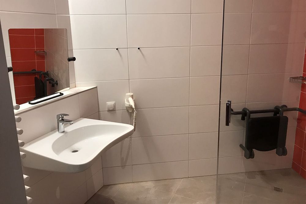 Öffentliche Toilette mit weißem Waschbecken, Spiegel, roten Fliesenakzenten und an der Wand montiertem Abfalleimer