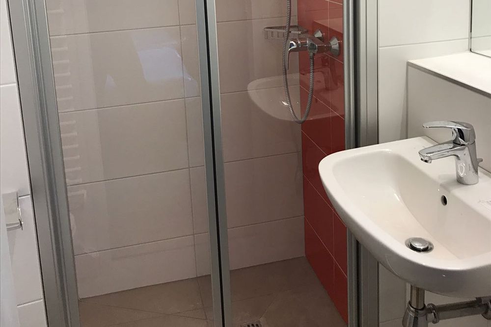 Kleines Badezimmer mit Glasdusche, weißem Waschbecken und roter Fliesenakzentwand.