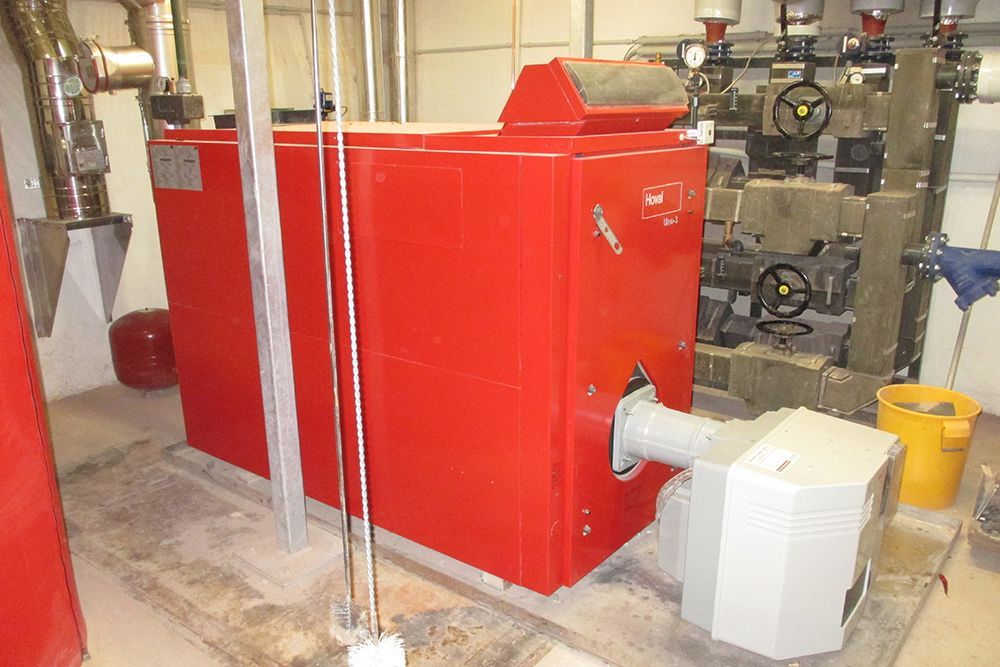 Ein roter Industriekessel mit grauen Rohren und einer kleinen weißen Pumpe in einem Hauswirtschaftsraum.