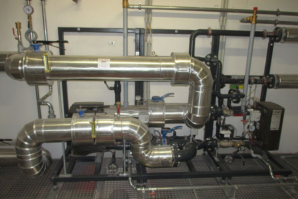 Industrielle Rohrleitungs- und Maschinenanlage mit glänzenden Metallkanälen in einer Werkstatt/einem Labor.