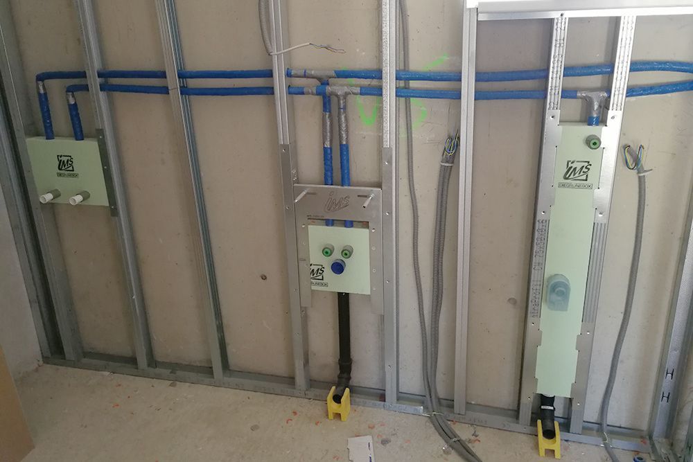 An einer unfertigen Innenwand mit freiliegender Rahmenkonstruktion sind elektrische Schalttafeln und Leitungsrohre