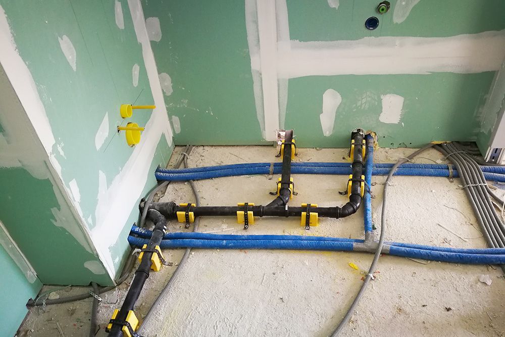Teilweise fertiggestellter Raum mit freiliegenden blauen und schwarzen Wasserleitungen vor grüner Gipskartonwand.