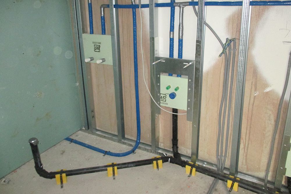 Elektrische Leitungen und Rohre wurden in einer unfertigen Wand verlegt, blaue und schwarze Kabel befinden sich in Bodennähe.