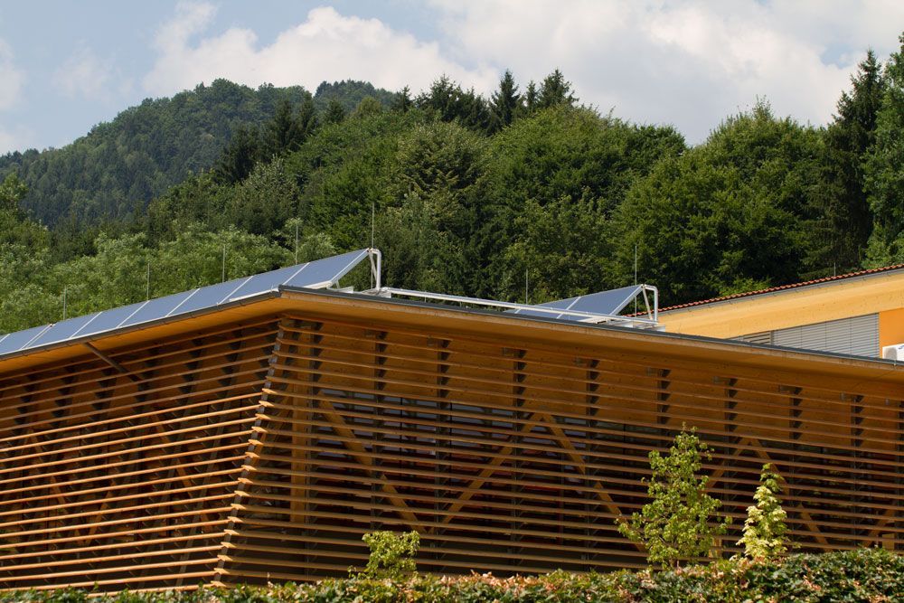 Modernes Holzgebäude mit Lamellenfassade und Solarpaneelen vor grüner Hanglage