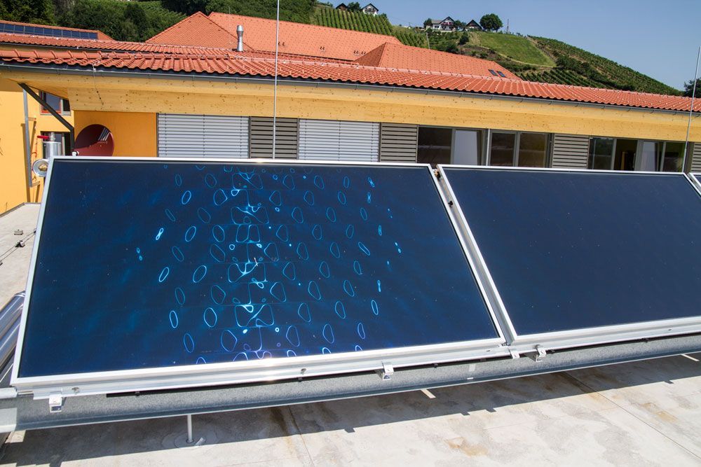 Solarthermische Paneele auf einem Dach, im Hintergrund ein gelbes Gebäude mit rotem Ziegeldach.