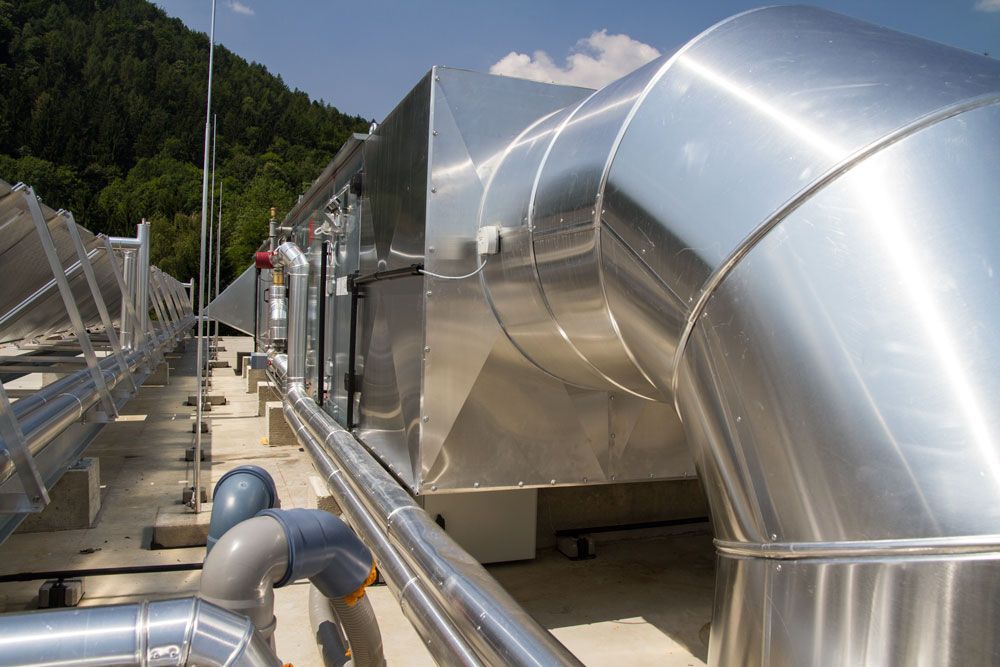 Industrielle Dachlüftungsanlagen mit großen, glänzenden Metalllüftungsöffnungen und Rohren unter klarem Himmel