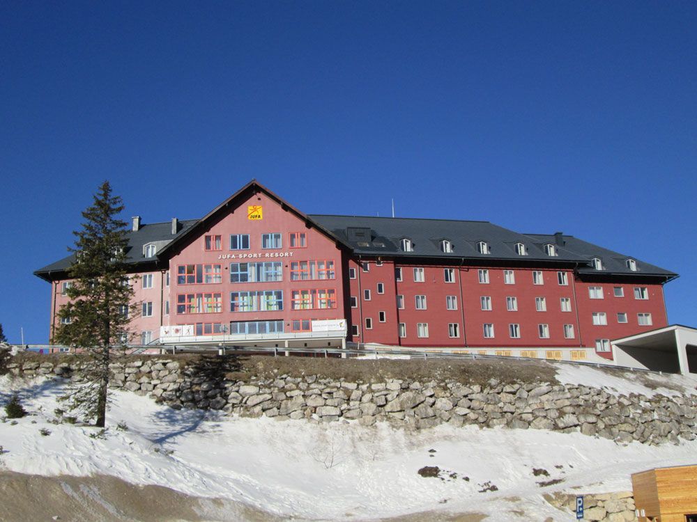 Rosafarbene Berghütte mit Steinmauer in verschneiter Landschaft unter klarem, blauem Himmel