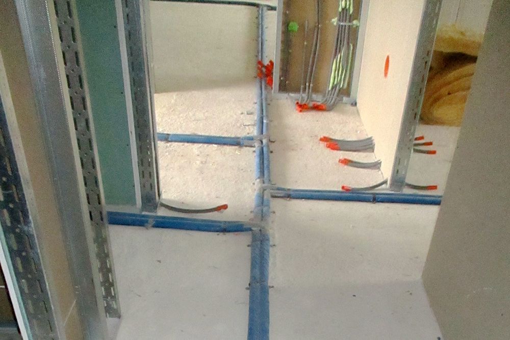 Innenansicht einer Baustelle mit blauen Klebebandmarkierungen an weißen Wänden und Boden,