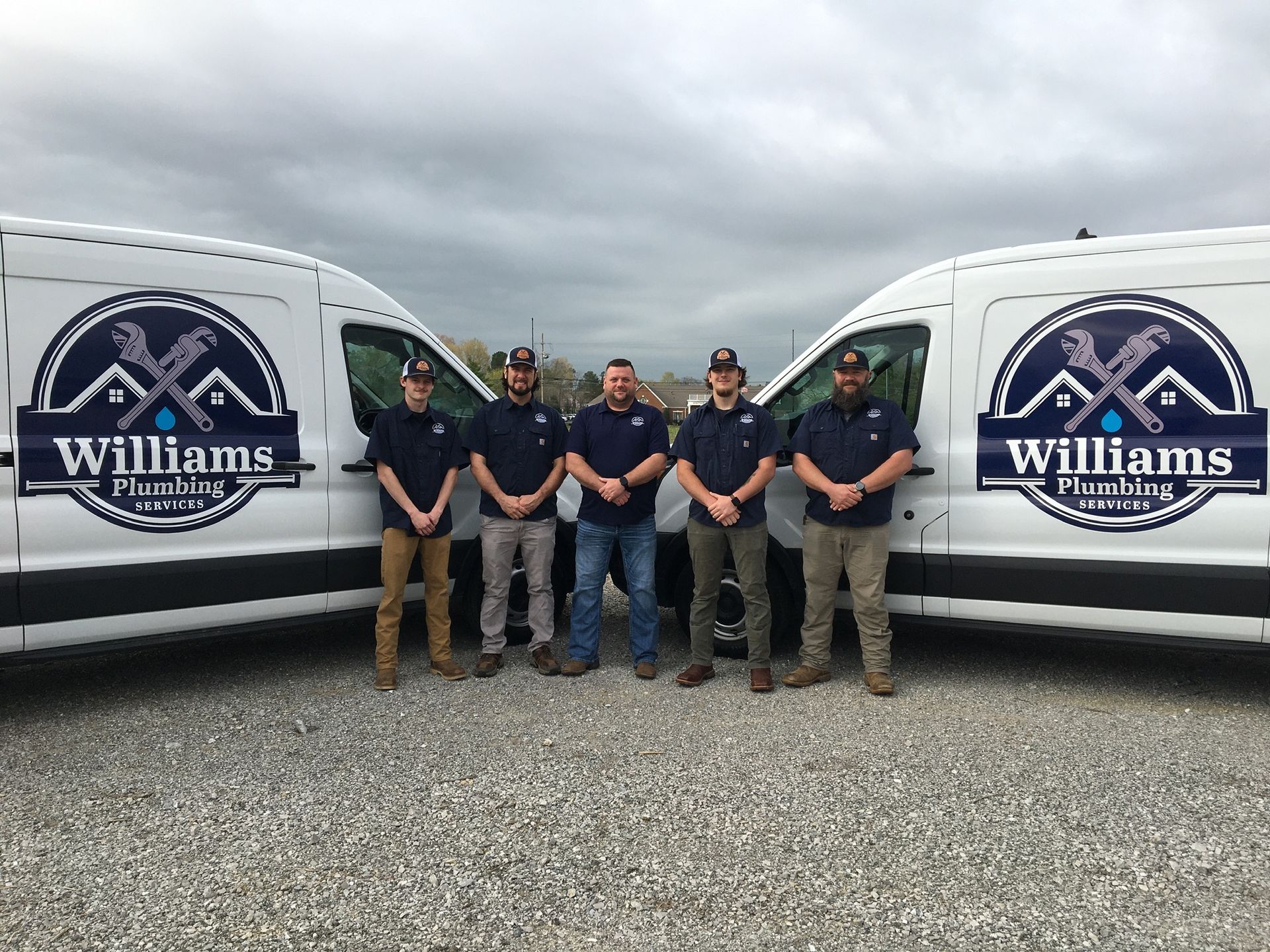 Five plumbers standing in front of two white vans with