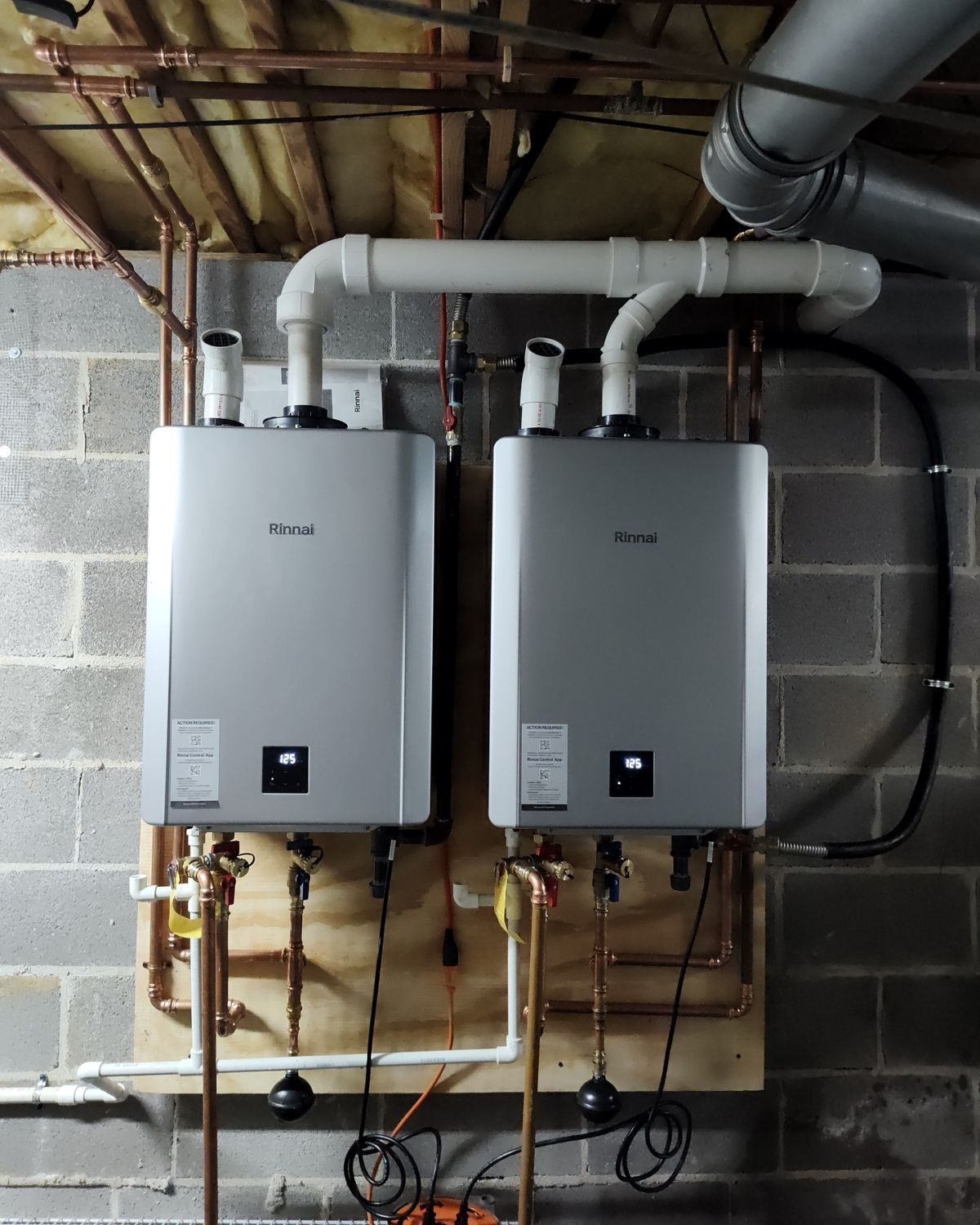 Two water heaters are mounted to a brick wall