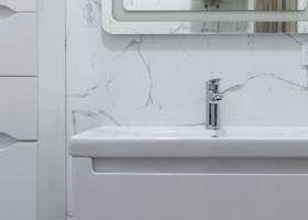 White bathroom sink with a chrome faucet, marble-patterned wall, and a mirror.