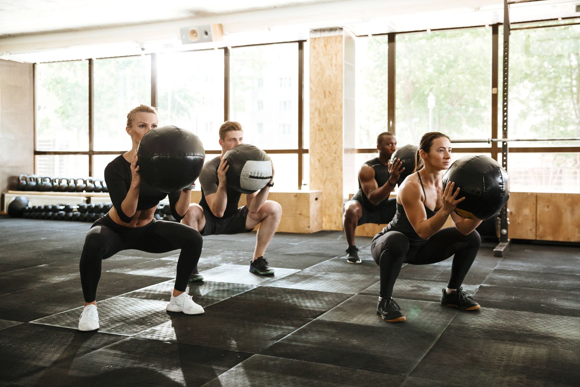 People doing medicine ball squats in a bright gym studio