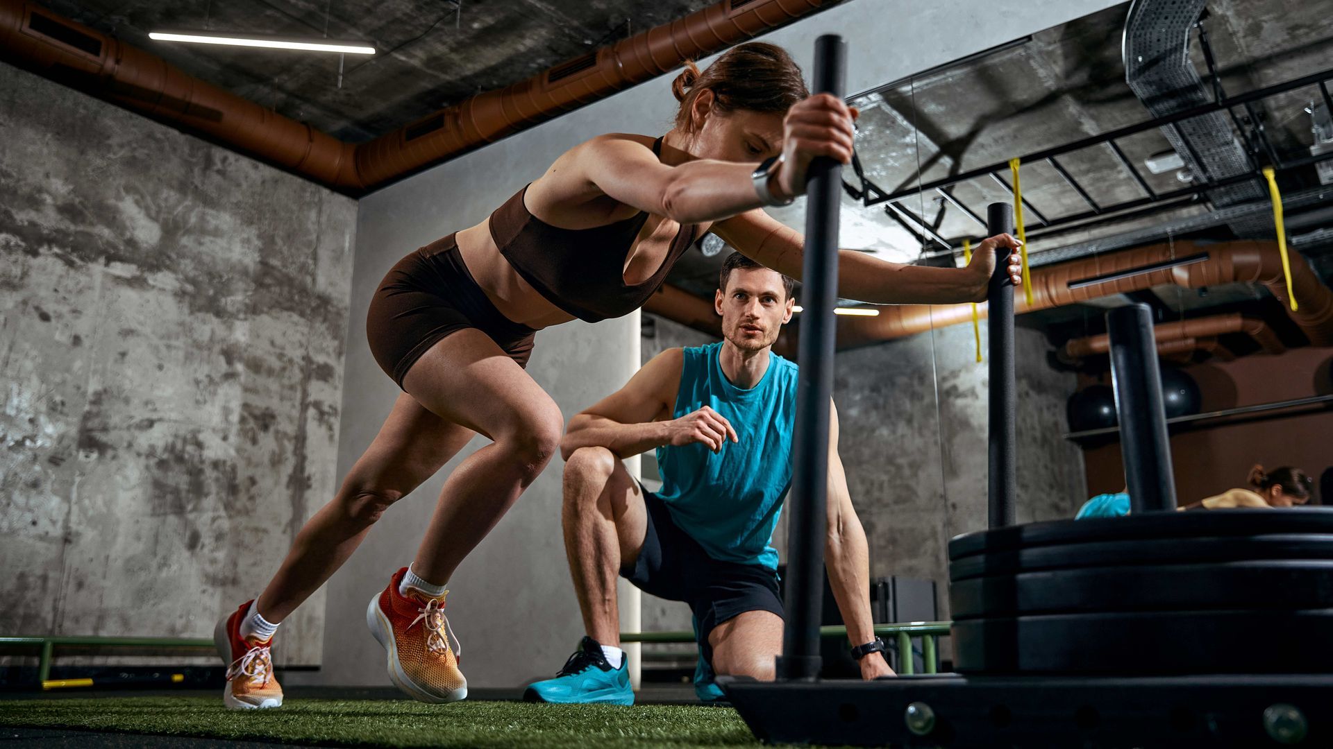 Athlete doing sled push in a gym while a trainer watches nearby