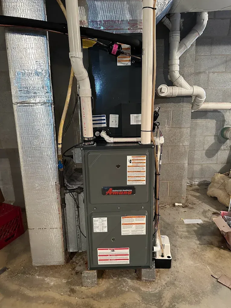 A furnace is sitting in a basement next to a brick wall.