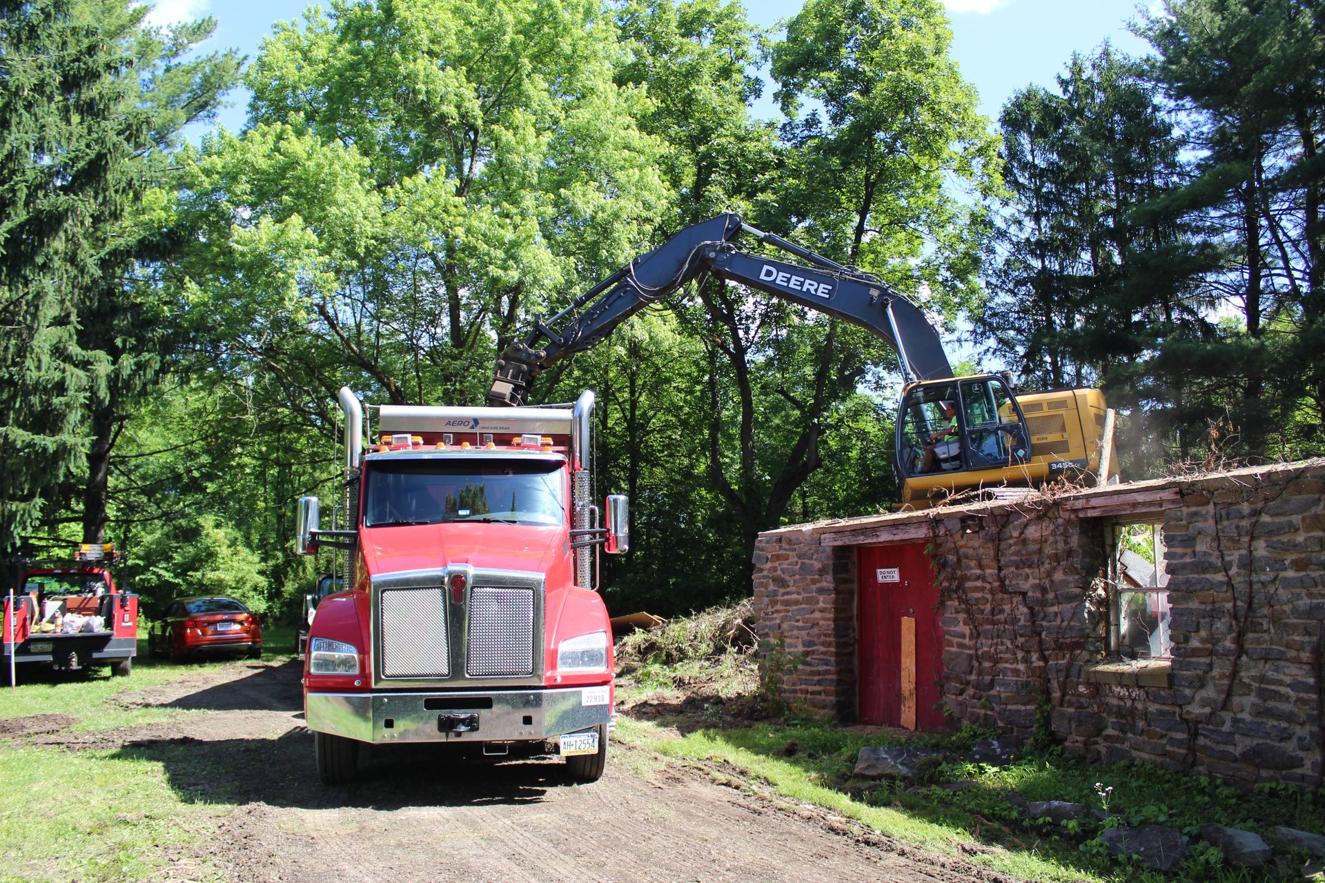 A red truck is driving down a dirt road next to a yellow excavator.