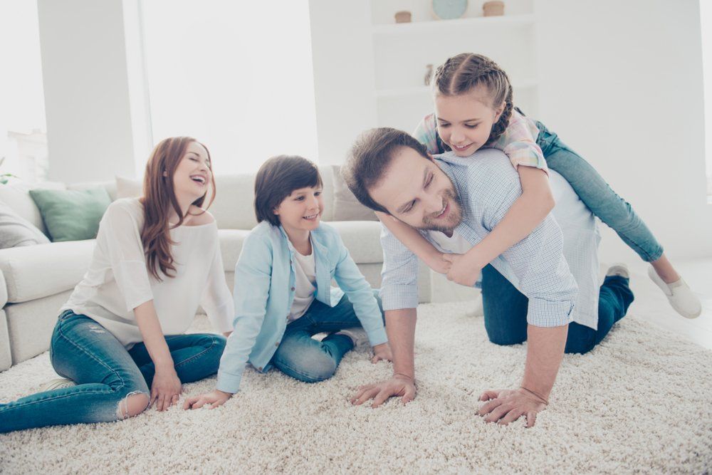 Happy Family Sitting On A Carpet Floor — Geoff Thompson's Independent Flooring Centre In Laurieton, NSW