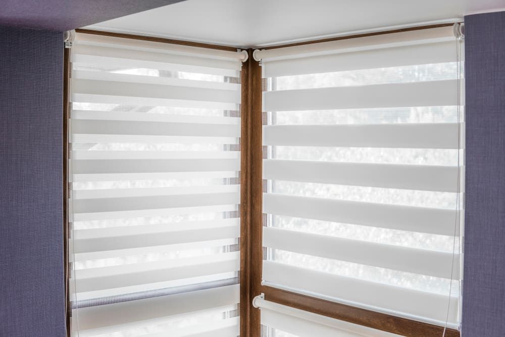 A pair of white blinds on a window in a room.