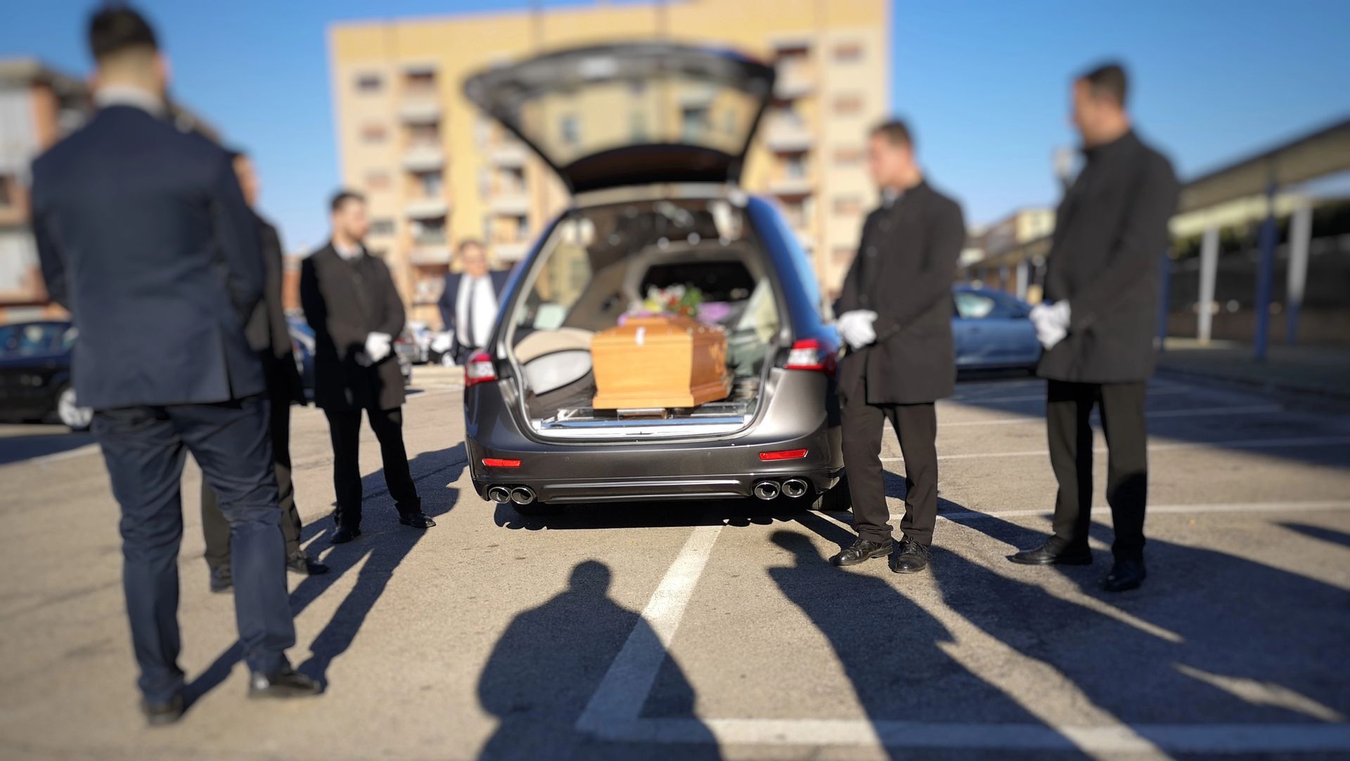 Alcune persone sono in piedi intorno al bagagliaio aperto di un'auto funebre