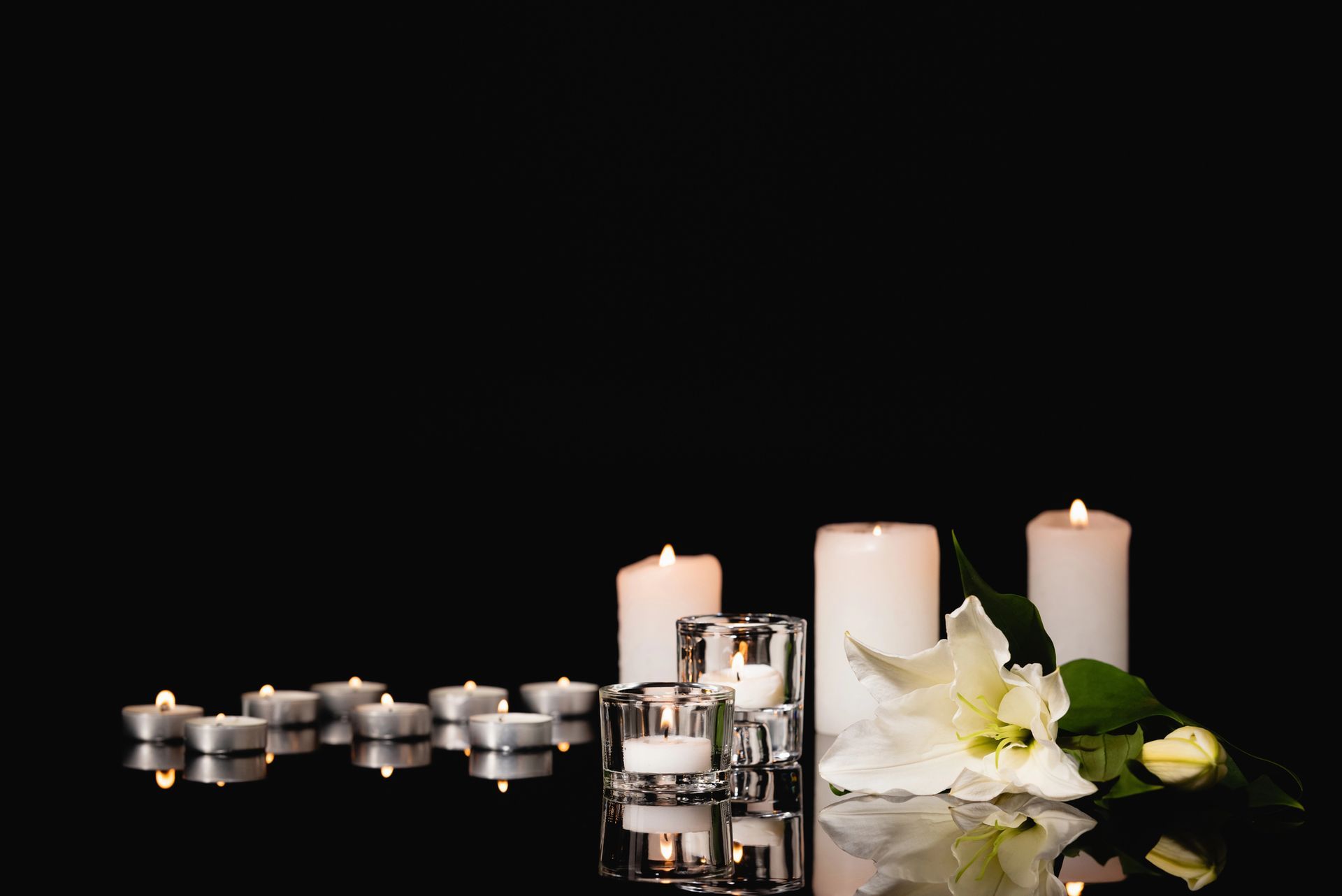 Candele bianche e orchidee accanto a portacandele argentati su una superficie nera riflettente.