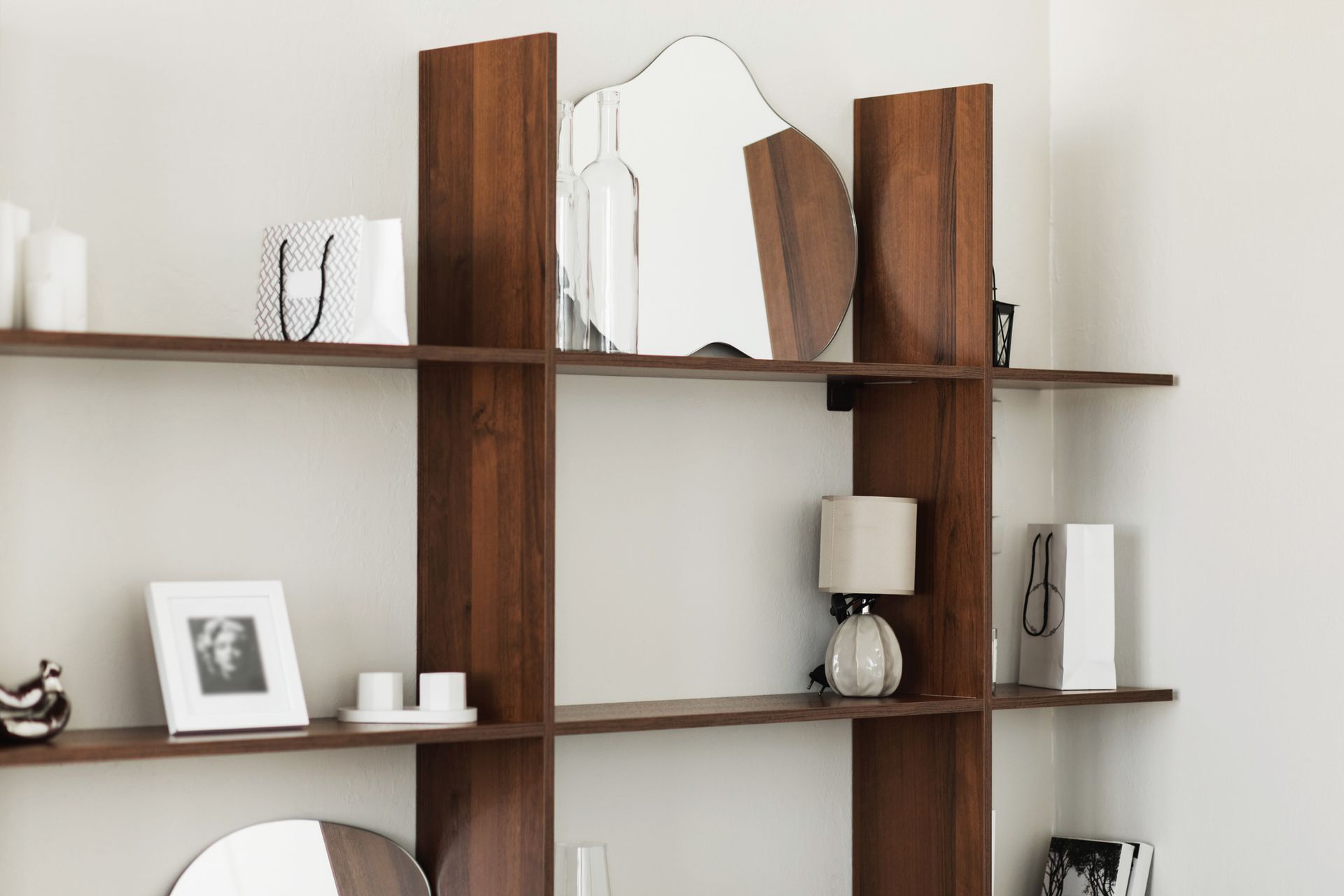Scaffale in legno con elementi decorativi, tra cui uno specchio, una lampada e delle candele, contro una parete bianca.