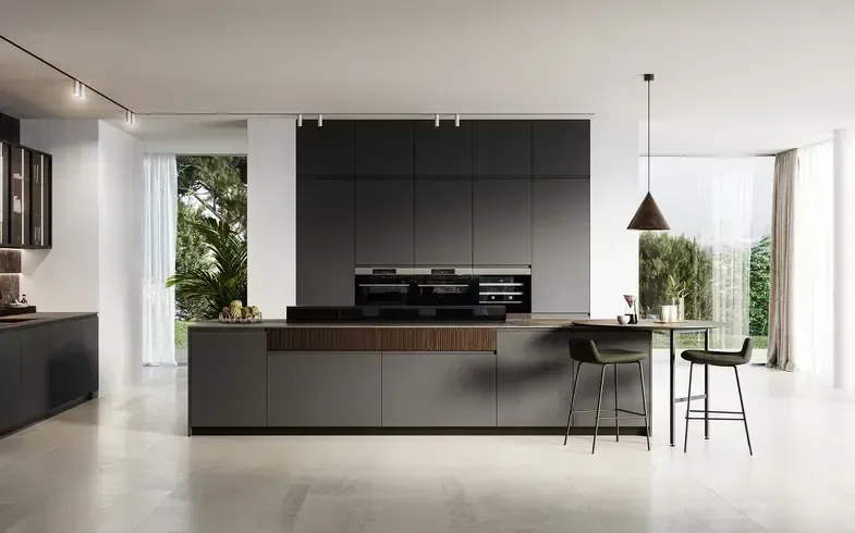Moderna cucina grigia con ampia isola e forni integrati. Accanto all'isola si trova una zona pranzo con tavolo e sgabelli da bar.