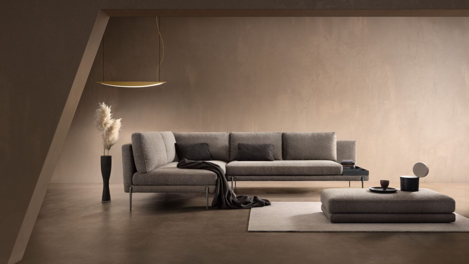 Soggiorno dai toni neutri con divano componibile, pouf e arredamento moderno. Un vaso nero contiene piante secche.