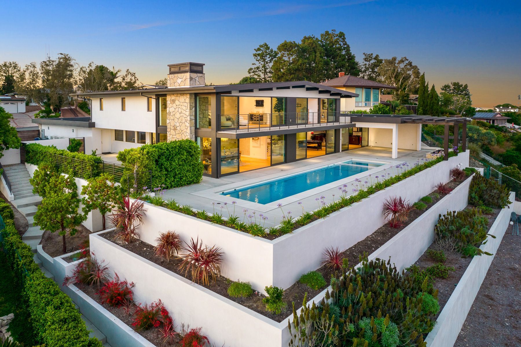 Photo showing an upscale home from a drone's point of view, the home is two stories and has plenty of glass in the back, as well as a simple, long pool