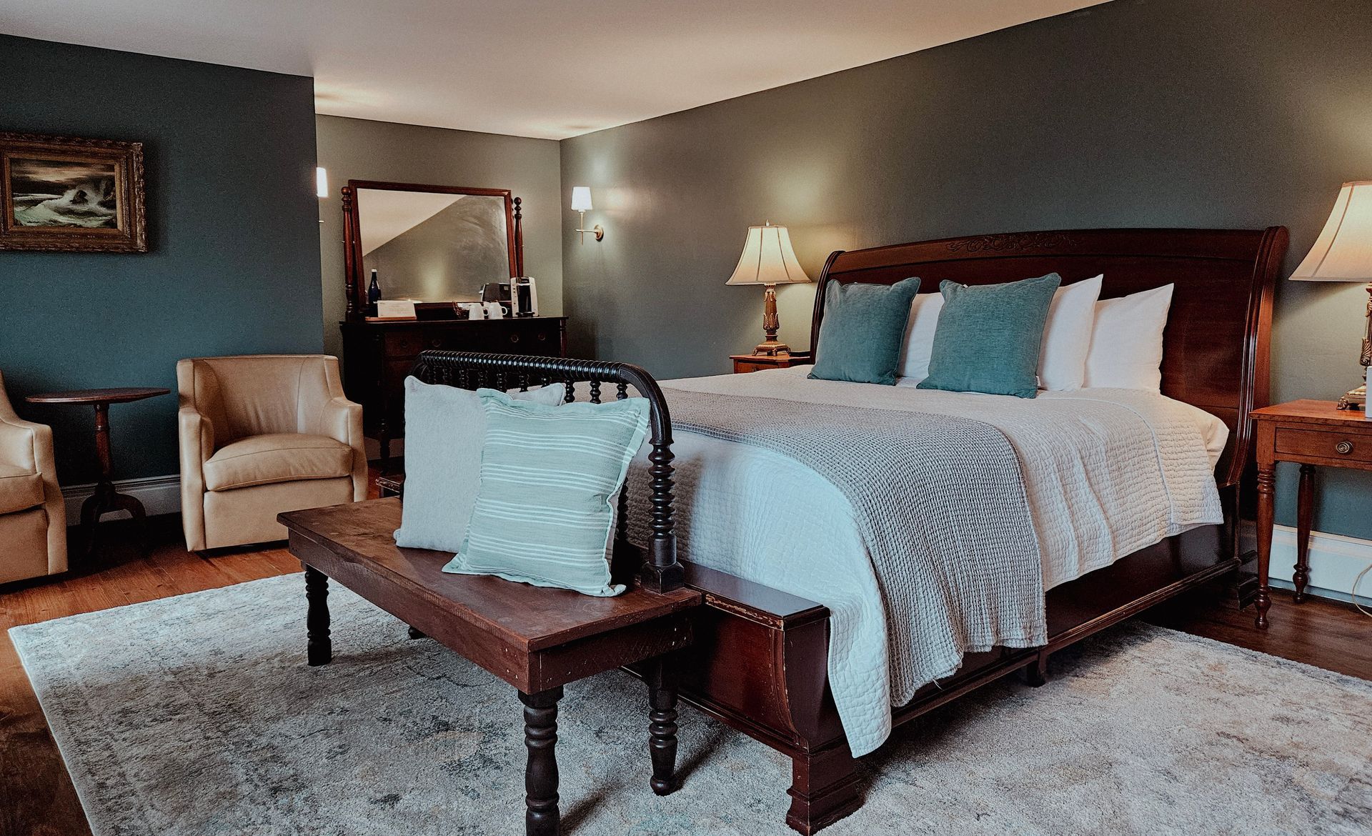 Cozy bedroom with a wooden bed, bench, armchair, mirror, and lamp in soft neutral tones