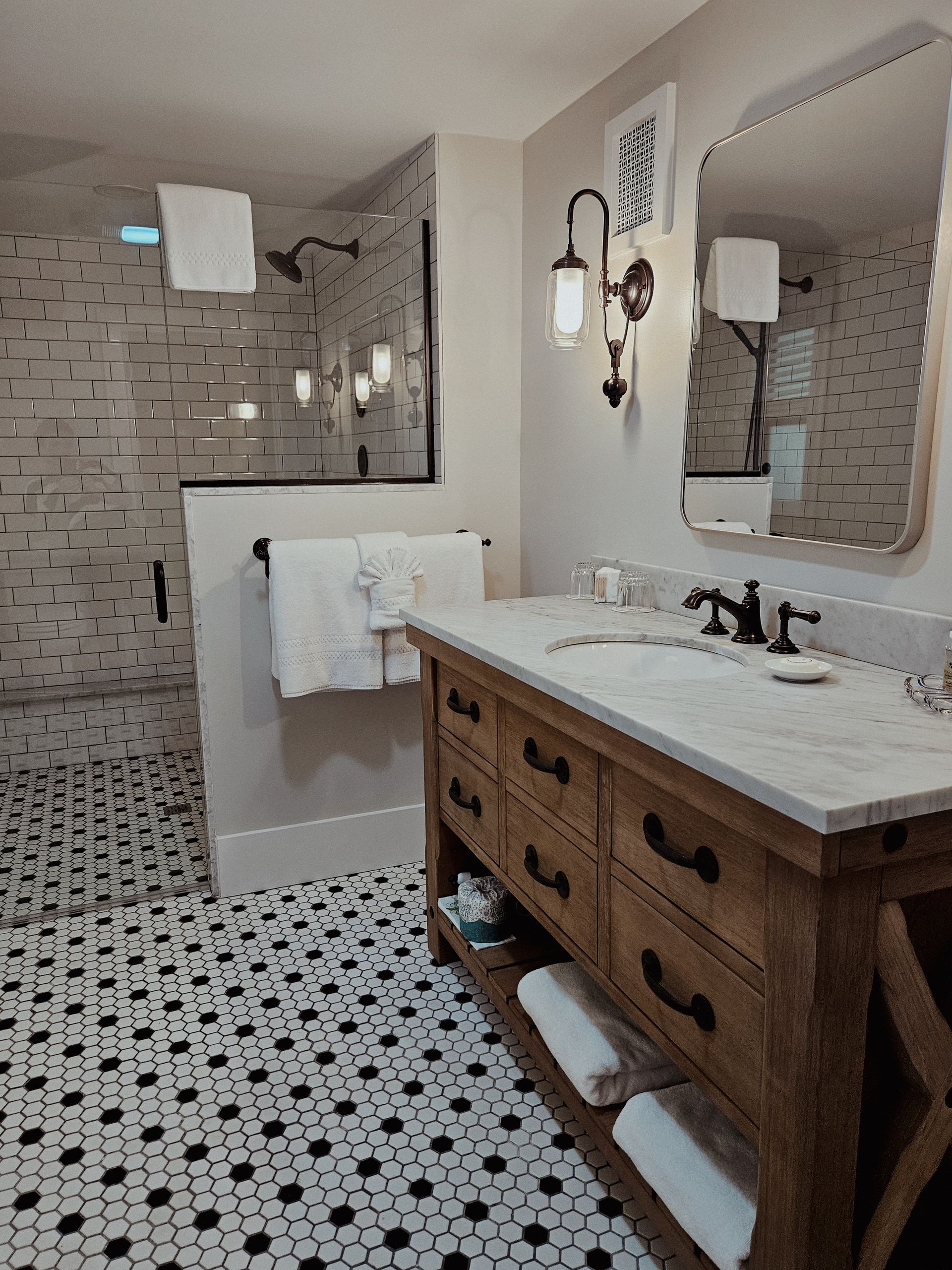 Bathroom with patterned tile, glass shower, wooden vanity, and marble countertop.