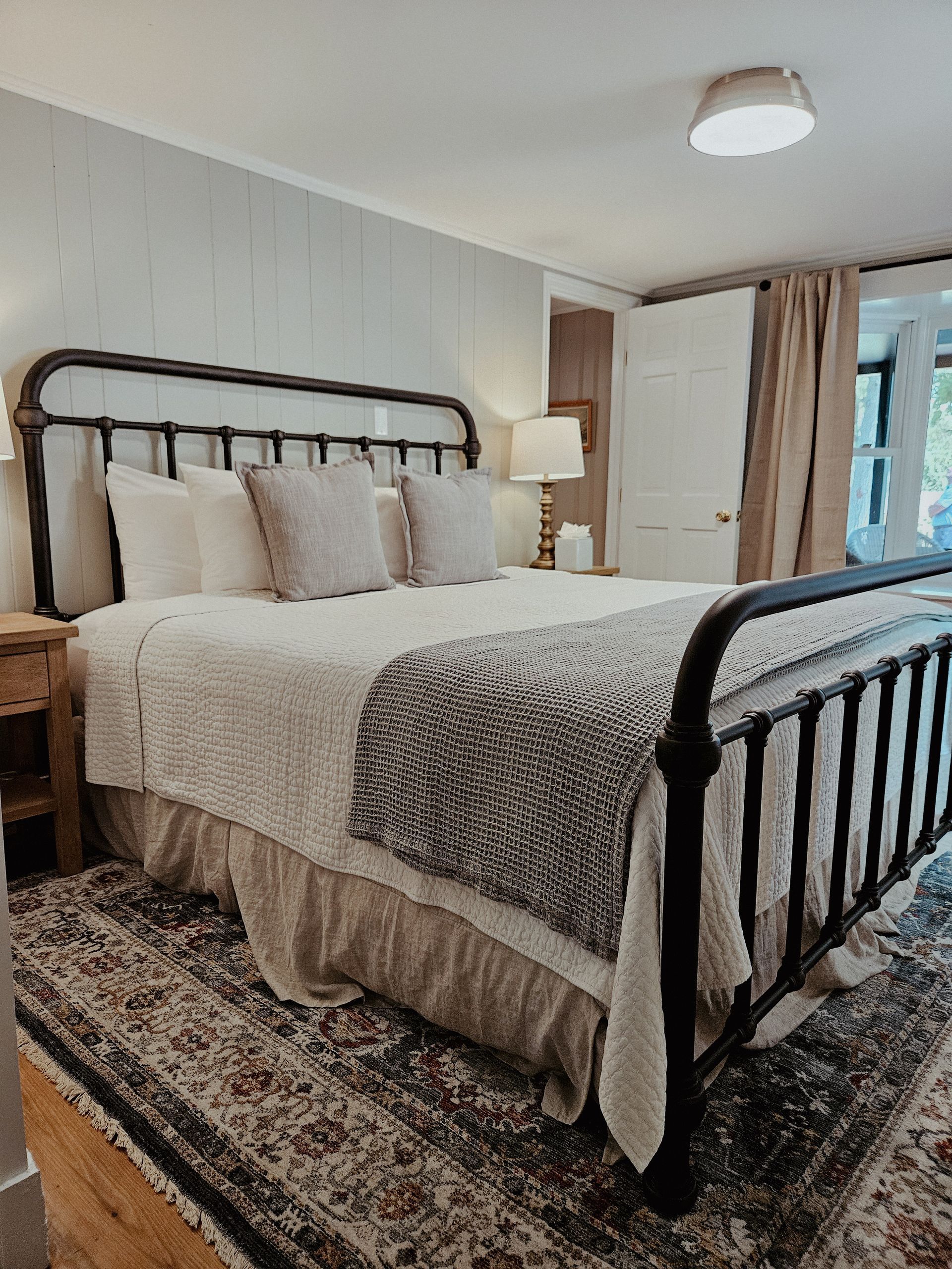 Cozy bedroom with black metal bed frame, beige bedding, patterned rug, and a window with curtains