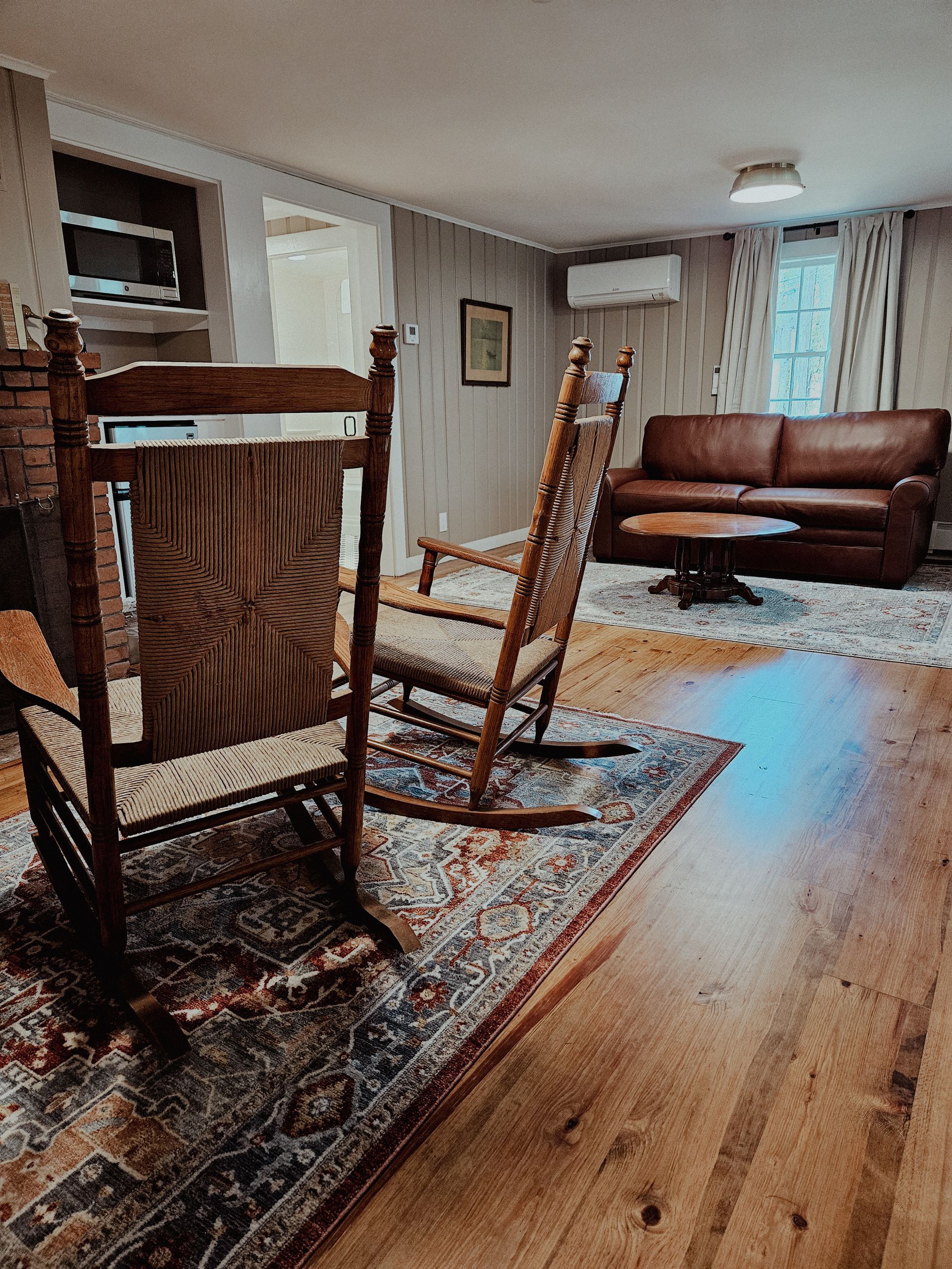 Living room with wooden dining chairs, a brown sofa, patterned rug, and hardwood floor