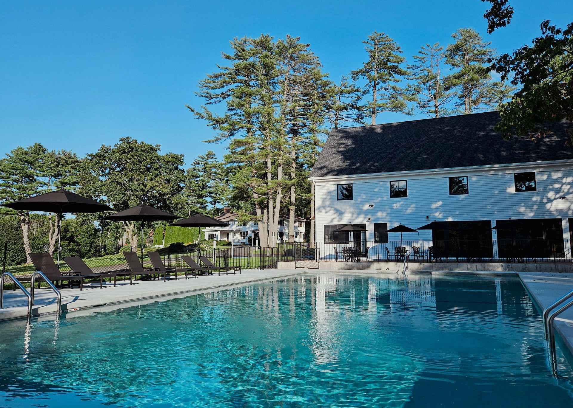Outdoor pool beside a white building and lounge chairs under a clear blue sky