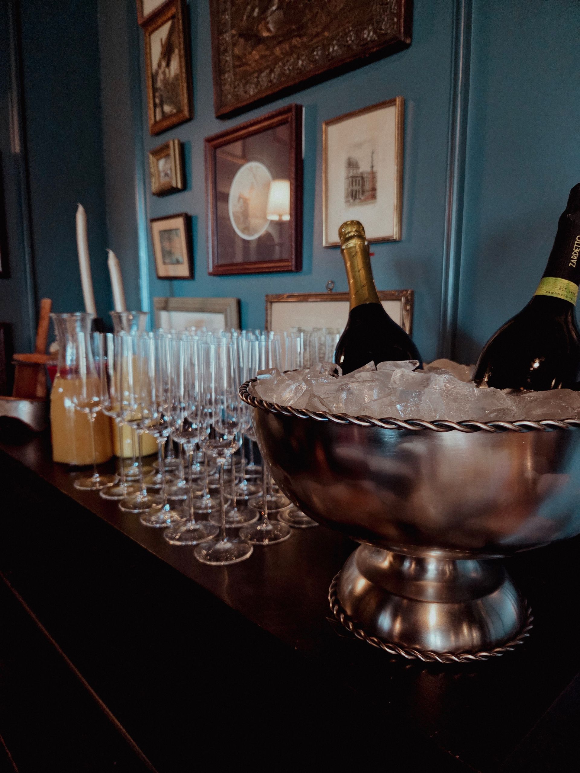Champagne bottles, glasses, and an ice bucket arranged on a bar with framed art on the wall