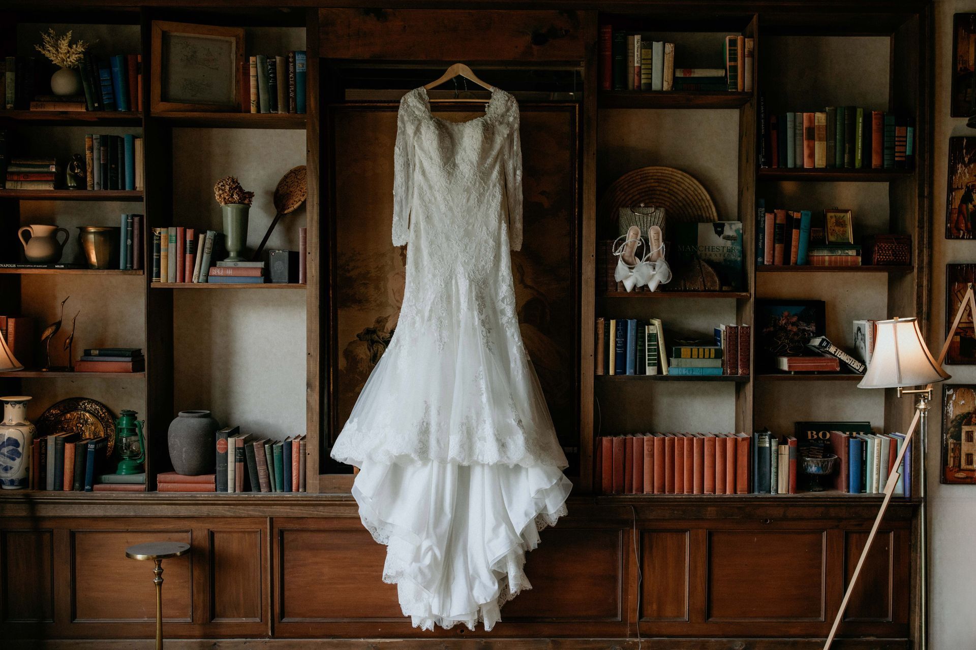 White lace wedding dress hanging in a wooden bookshelf-lined room